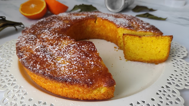 foto di una ciambella di torta all'arancia con una fetta tagliata e delle arance tagliate sullo sfondo bianco marmo