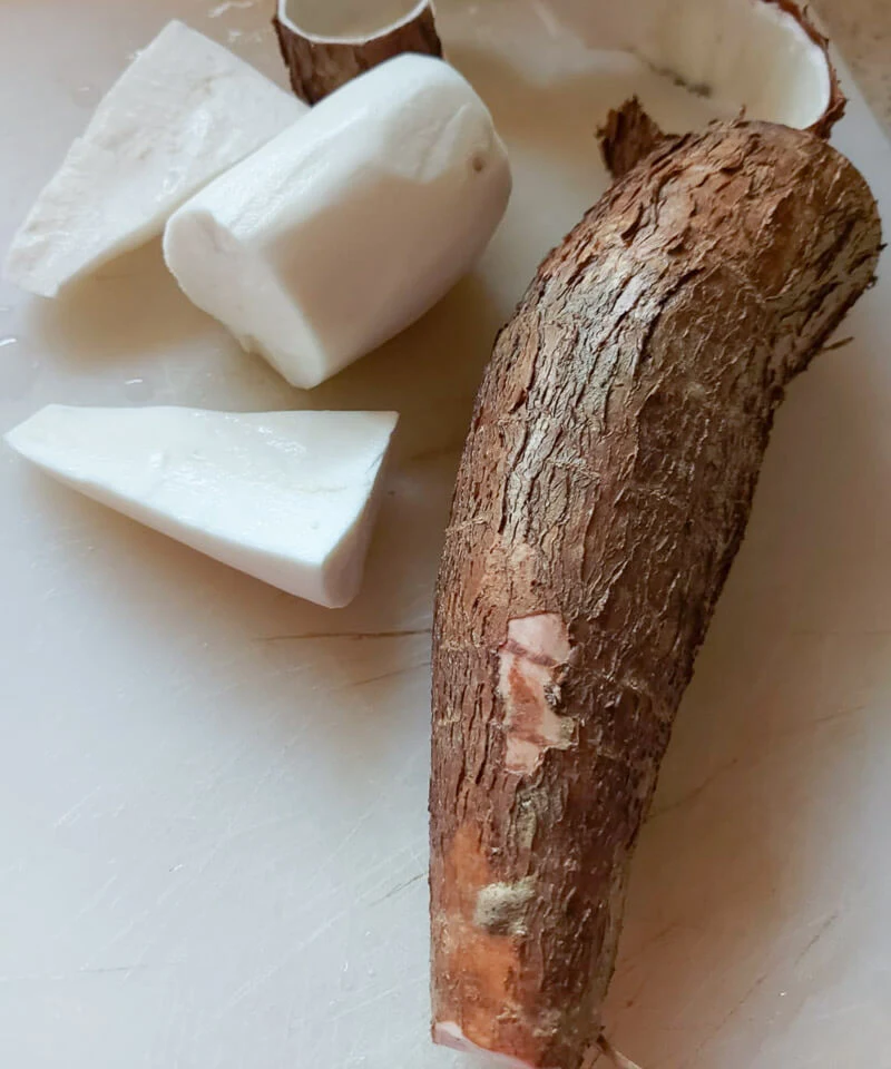 Fresh cassava, with skin on and peeled on a white cutting board.