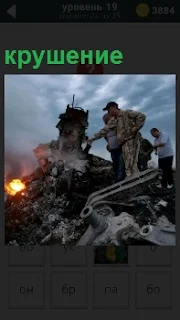 Люди ходят среди обломков крушения и огня. Разбросанные во все стороны фрагменты различных деталей 