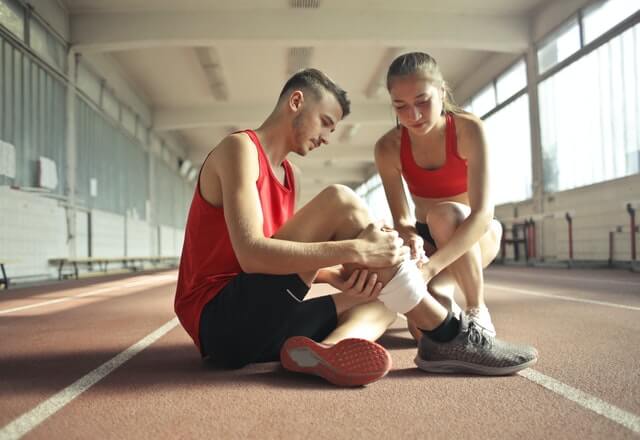 Lesiones al correr: chico sentado en el suelo de una pista de atletismo y tocándose un tobillo por sentir dolor