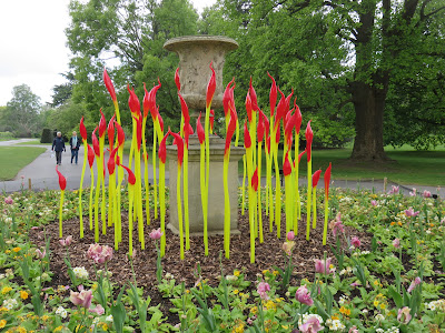 photo of Chihuly glass sculpture of red and yellow 'paintbrushes' or bullrushes, in a flowerbed