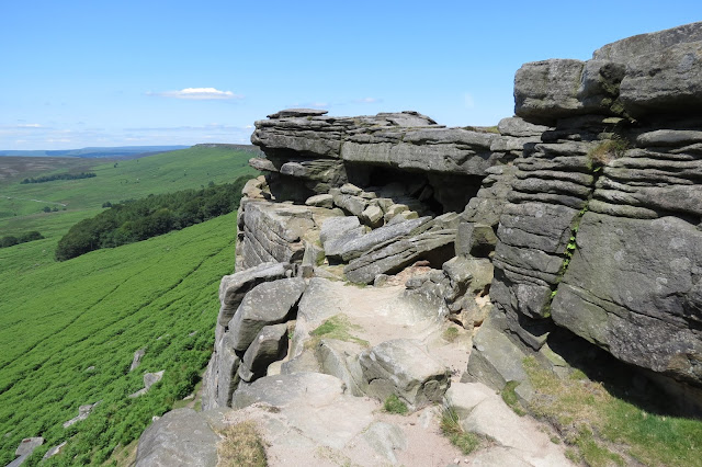 A small, sandy ledge just below the escaprment. Moorland and trees below.