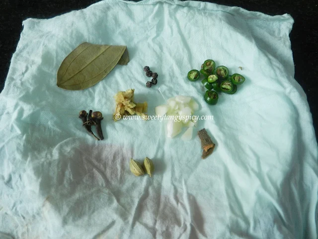 Aromatic spices, including a bay leaf, cardamom pods, cinnamon sticks, black peppercorns, chopped ginger, chopped green chili, and garlic cloves, artfully placed on a clean white muslin cloth.