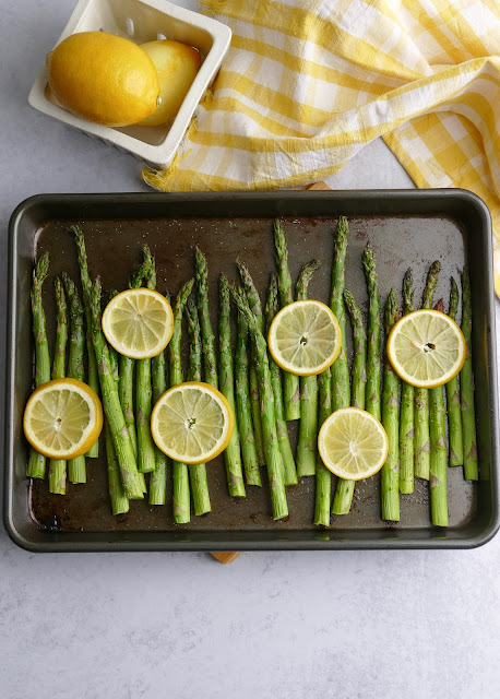 asparagus on a sheet pan with sliced lemons on top.