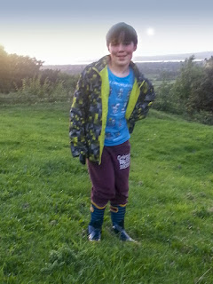 Boy wearing Bogs Wellies, standing on a hill. 