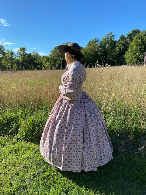 the author in a purple printed 1860s dress and gray felt hat standing in a field