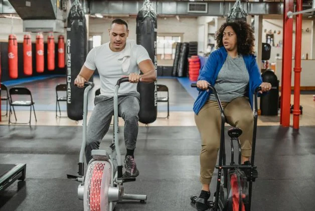 Man and woman doing stationary cycling as part of low impact HIIT exercises