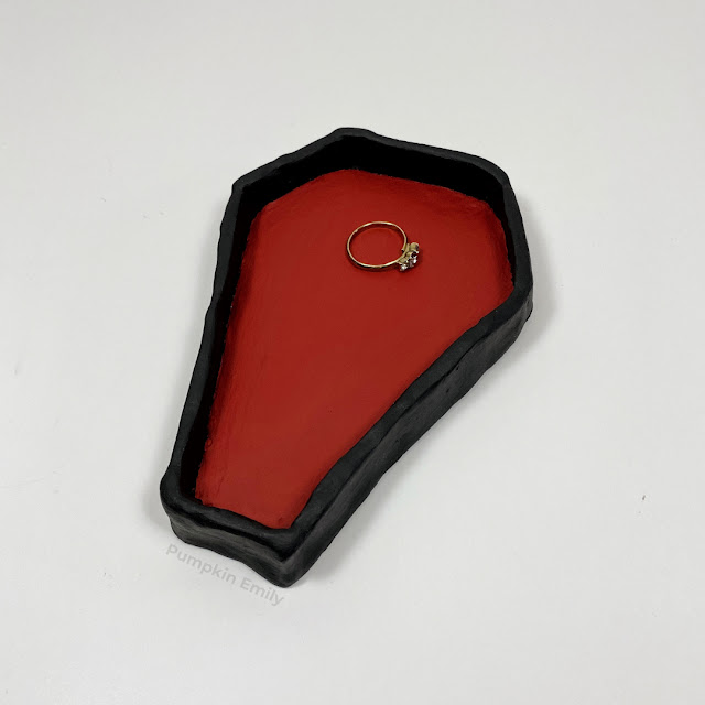 A red and black coffin jewelry dish made out of air dry clay.