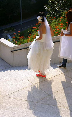 Picture of a bride lifting up her dress to show off her glowing orange shoes; or maybe to walk down the stairs without tripping or dirtying her hem