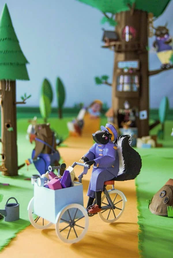 detailed diorama scene made of paper showing skunk dressed in uniform pedaling delivery tricycle