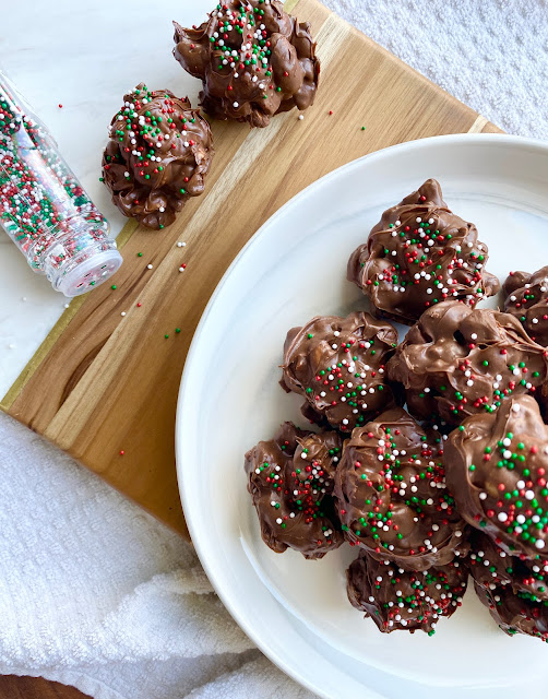 Plated peanut clusters on a white plate and wooden cutting board with jar of sprinkles.