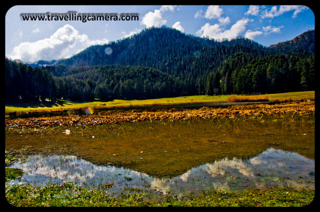 My adventurous self finally took over this March and I headed to the hills. Dalhousie beckoned me with its tantalising name and fame. During my three days two nights stay in Dalhousie, I stole a day to visit Khajjiar and Chamba. I am so glad that I did. Khajjiar is unbelievable. Who would have imagined this expansive pastureland surrounded by Deodars right in the middle of a Very Hilly Terrain.
When I reached there, blissfully, there wasn't much crowd. Usually, the entire ground is full of people. In this paricular Picture, the absence of human activity helps in emphasizing the magnificient Deodars.A close up of Deodars. Look at the two men on the left to get an idea of the sizes of these giant trees.A Colorful bridge leading up to the middle of the lake.Hills reflected in the water of the lake. Me on the Bridge. My guide obliged me with by clicking this picture.A horse grazing peacefully. I don't think I have ever got so close to one except at weddings.Another Horse. This one was rather skinny though considering the amount of fresh grass it has access to.Cloud rising out of the hills reflected in the lake. There were several beautiful buildings around the ground. Many of these were restaurants.Me next to a broken bridge. A Philosophical Setting.Chamba, Colorful, Hill Stations, Hills, Himachal Pradesh, Holidays, Lakes, Nature, Sky, Snow Covered Hills, Trek, Khajjiar: Posted by Vibha Malhotra on www.travellingcamera.com:Mesmerising Khajjiar