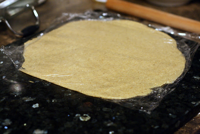 Flattened gluten free dough rolled out sandwiched between two pieces of plastic wrap.