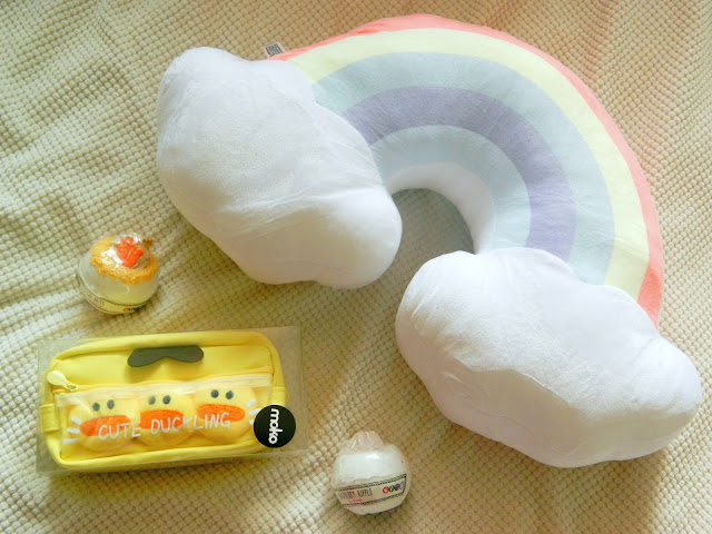 A photograph showing products from Kenji UK, a yellow fluffy duckling pencil case, a pastel rainbow cushion and two cute bathbombs