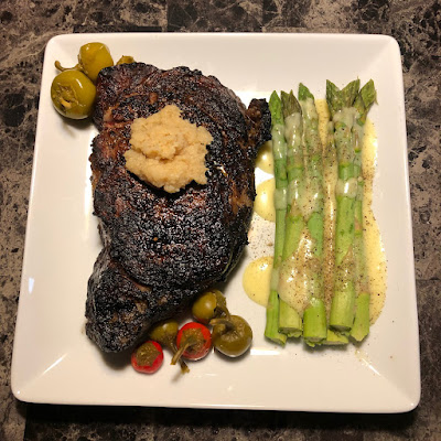 Thick cut ribeye steak grilled Pittsburgh rare along with some steamed asparagus with hollandaise