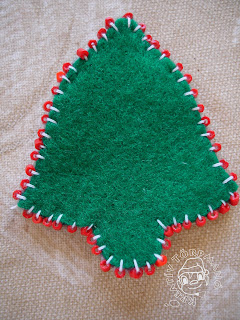 Szöveg: Oldalán gyöngyös karácsonyi csengő. Kép: Közelkép egy zöld sima csengőről, aminek a széleire piros gyöngyök vannak felvarrva fehér cérnával.