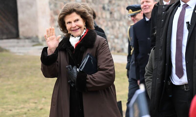 Queen Silvia wore a red poncho and red blazer pant suit. Gold leaf brooch and gold necklace. Governor Beatrice Ask