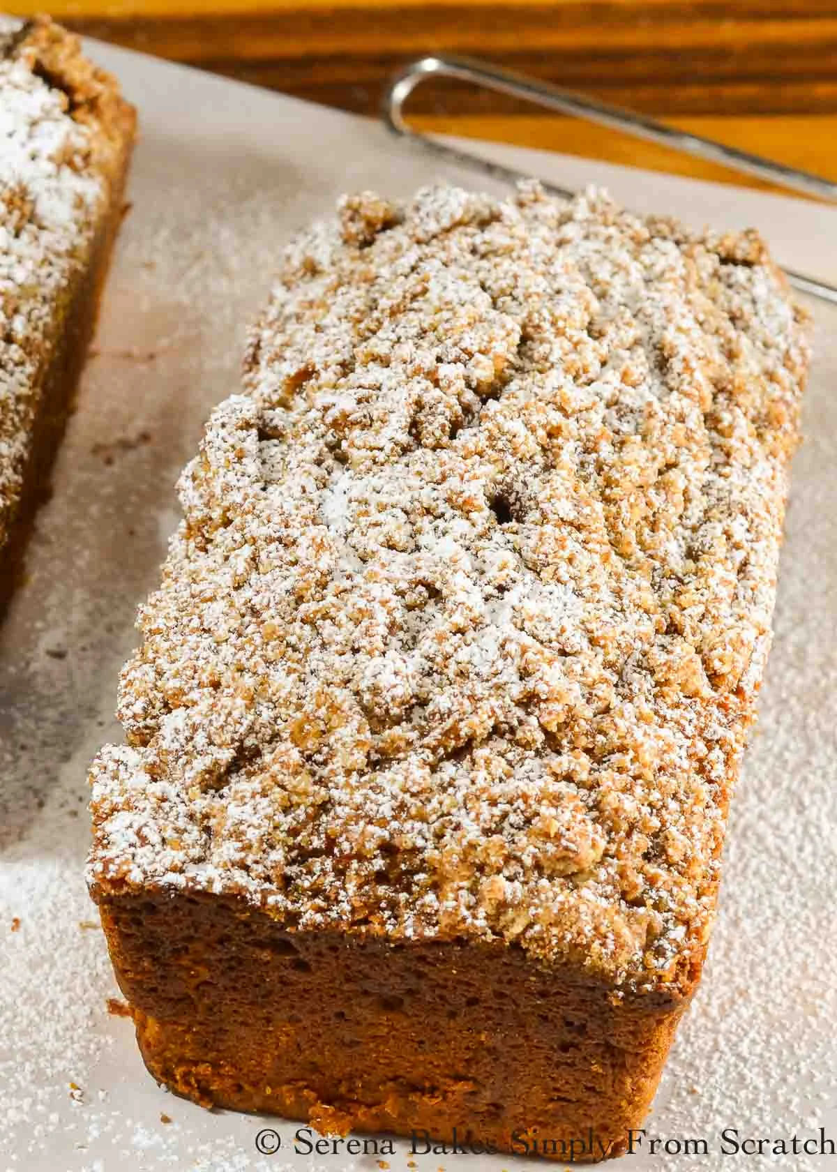 Pumpkin Bread with Streusel lightly dusted with powdered sugar on a piece of parchment paper.