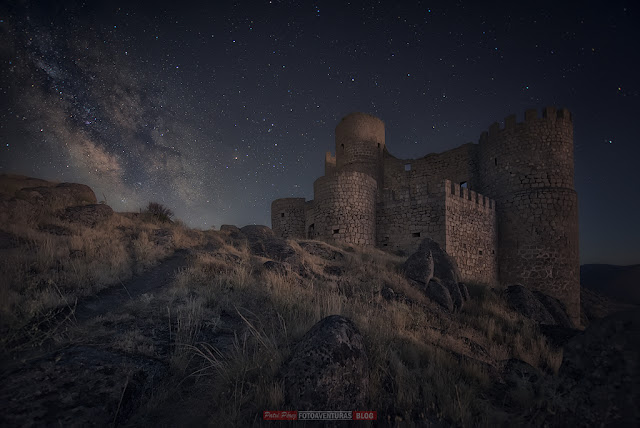 castillo en lo alto del camino rodeado de rocas con la vía láctea a su izquierda