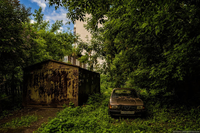 Ржавая машина припаркована у ржавого города под деревом