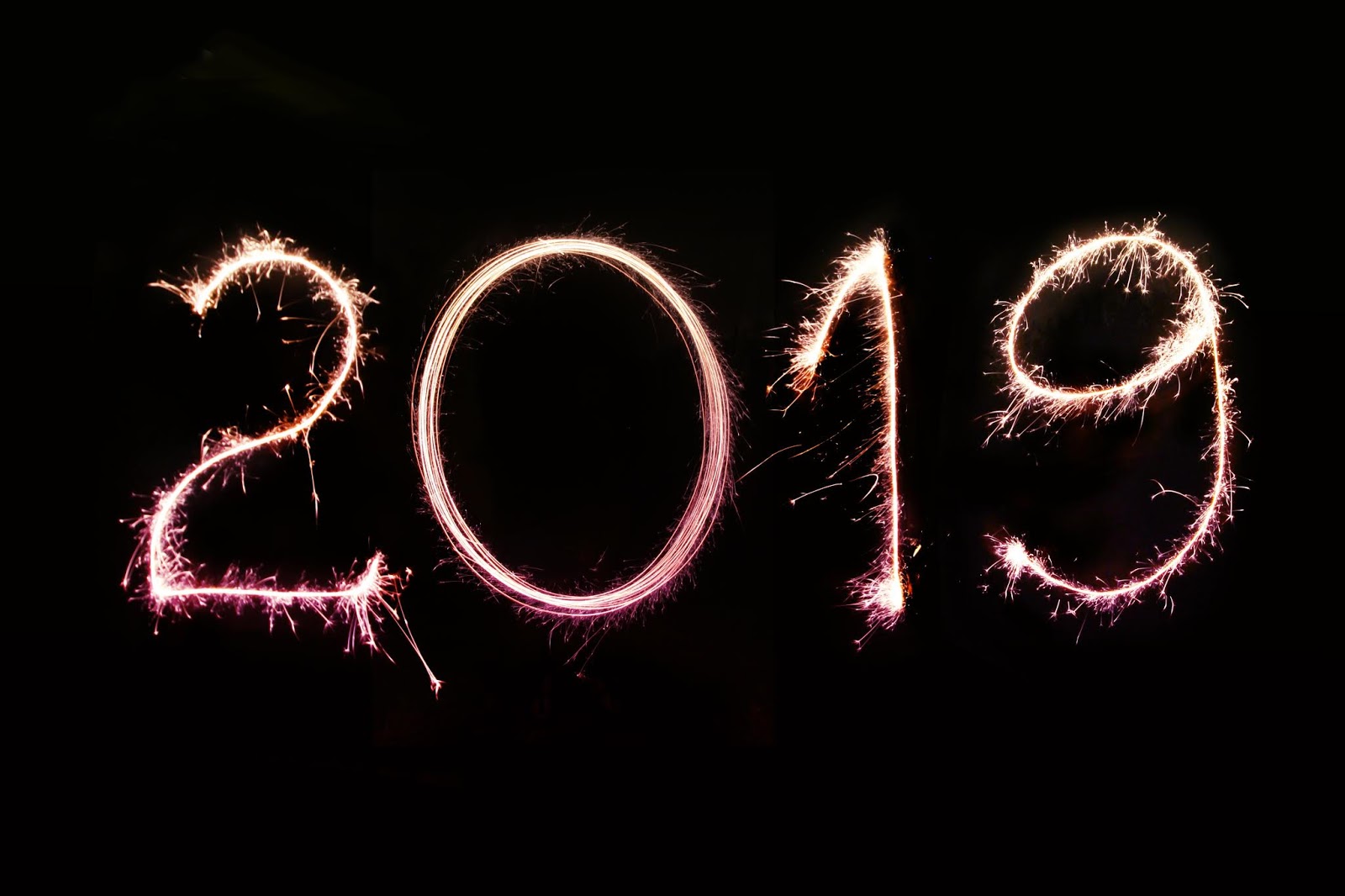 A photo of pink 2019 light art - like writing with a sparkler in the air - against a black background.