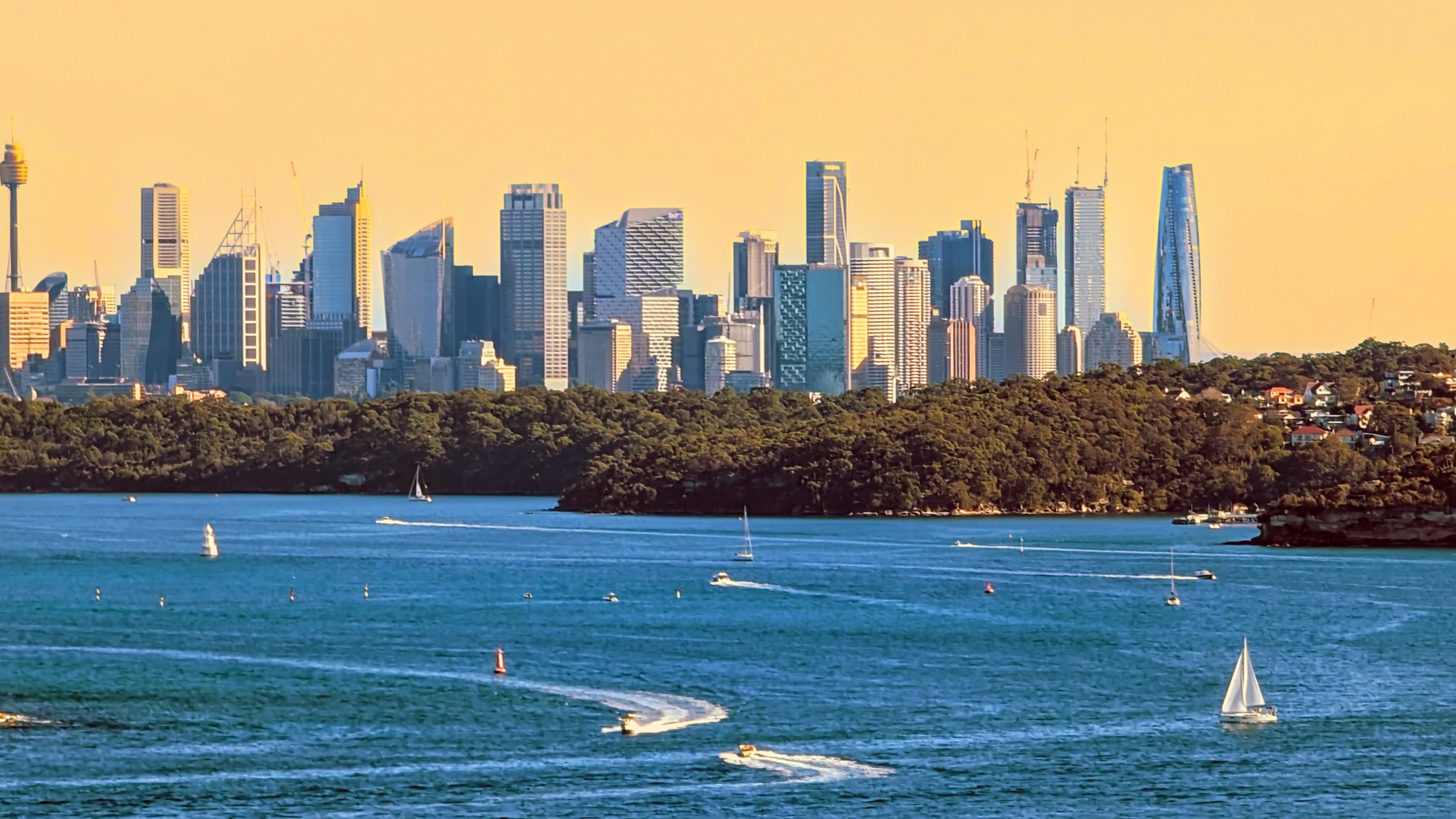 Edited landscape photo of Sydney Harbour with the city a false yellow sky, CBD tower blocks, and boats on the water.