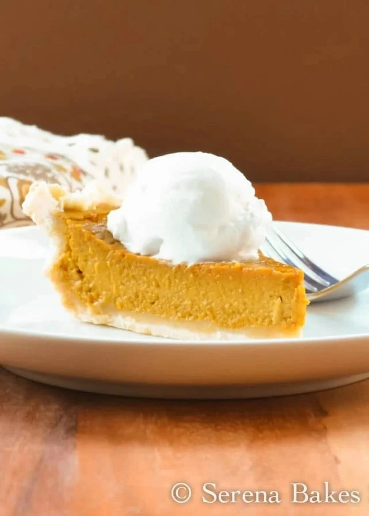 A slice of Dairy Free Pumpkin Pie on a white plate topped with coconut whipped cream.