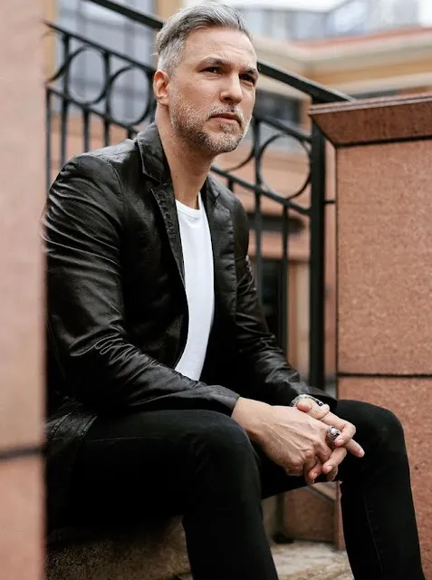 Handsome man wearing black leather blazer jacket sitting on bench outside