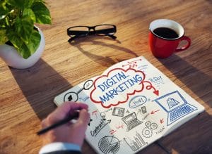 Digital marketing design and graphics on a brown table with eye glasses, potted plant and a red mug of coffee.