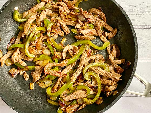 Steak and onions and peppers frying in a pan.