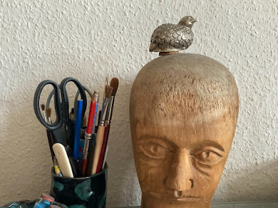 Bild aus dem Büro: Ein Metallvögelchen sitzt auf Perückekopf