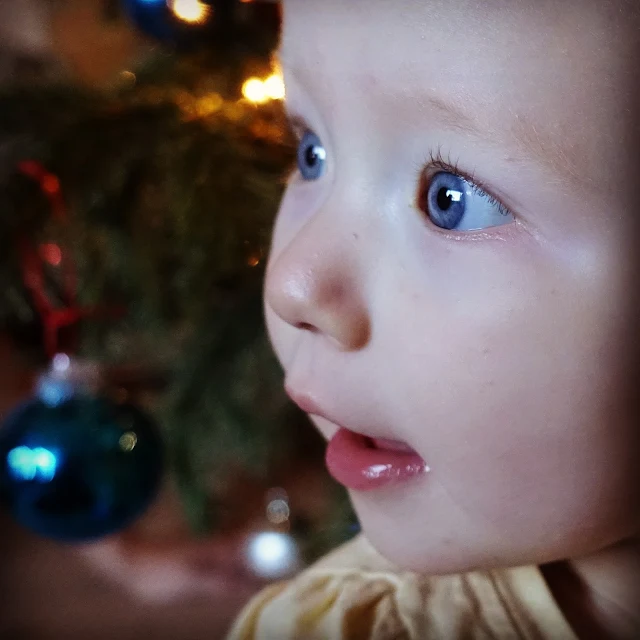 A blue eyed baby in front of a tree