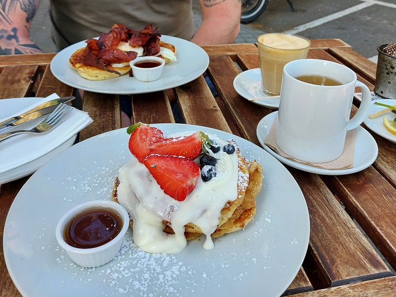 Cinnamon roll pancakes topped with cream cheese frosting and berries at Picnic, Barcelona - with bacon & egg pancakes across the table