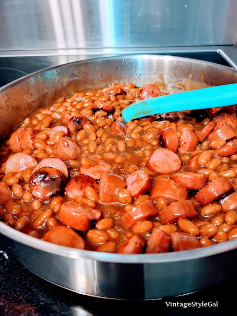 Smoked sausage and baked beans cooking in stainless steel skillet on stovetop