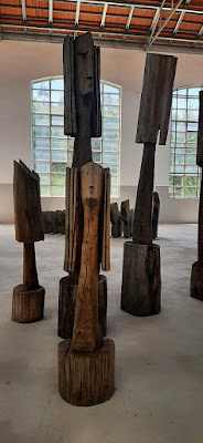 Esculturas em madeira em exposição e janelas ao fundo