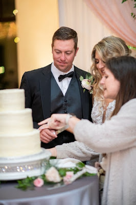 At Last Wedding planner showing bride and groom how to cut the wedding cake