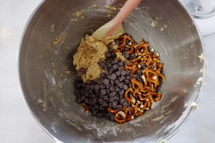 adding chocolate chips and pretzels to cookie batter