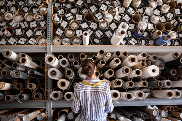 Female textile designer poses with fabric rolls in sustainable workshop.