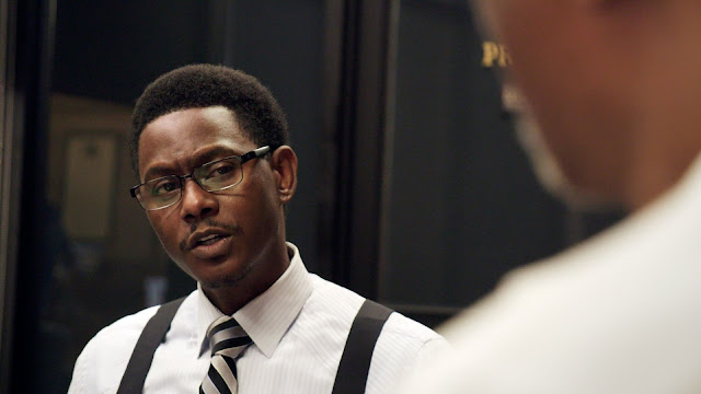 A Black man with suspenders talks to a client