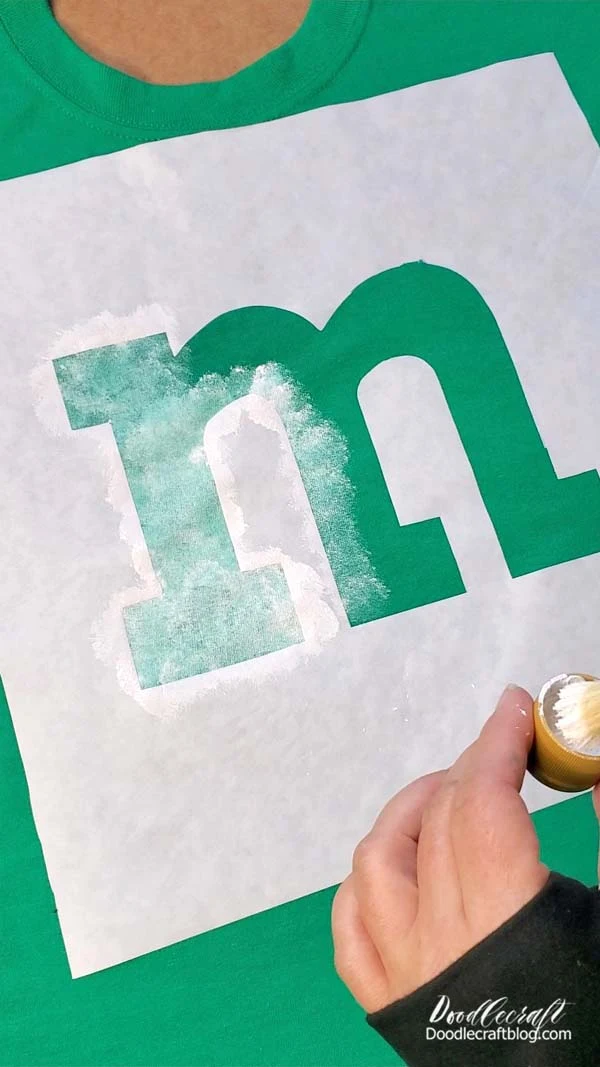 Step 4: Paint!  Now use the acrylic craft paint and stencil brush and fill in the M.   It does not need to be bright white.   Look at the opacity of an actual M&M, they aren't super white...so this is perfect, plus it will keep the shirt soft and not all stiff from paint.