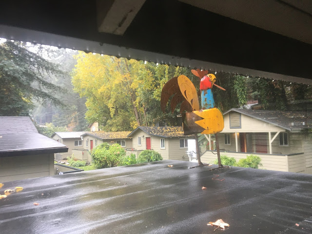 metal rooster sculpture in front of rainy cabin-style lodgings.