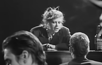 Kirsty MacColl leaning over piano, singing at Shane MacGowan, black and white, in Fairytale of New York,
