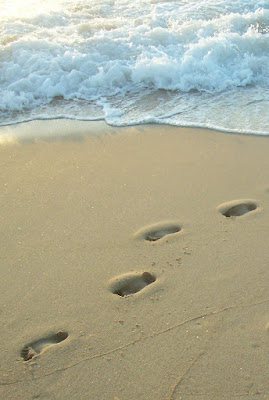 footprints in sand leading away from wave breaking on shore