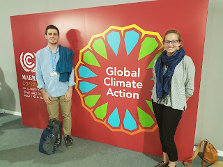 This image shows two students side by side in front of the COP22, UN Climate Change Negotiations Logo