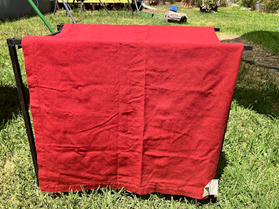 A large red piece of fabric is draped over an unseen structure in a grassy back yard. End ID.