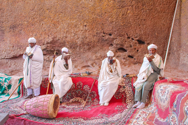 four men in traditional white cotton shawls praying in front of a church