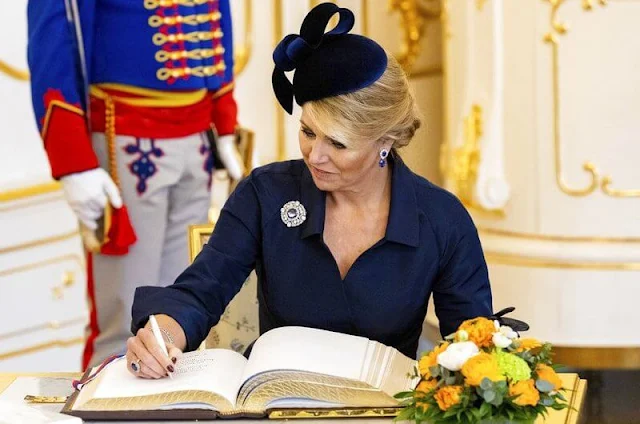 Queen Maxima's outfit, navy coat and dress, is from the fashion house Natan. Philip Treacy. President Zuzana Caputova