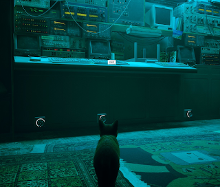 Screenshot from the game Stray. A cat sitting in front of a desk with ancient computers.