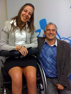 Mara,  de saia e blusa de lã, ao lado de Naziberto,de colete azul, blazer marron e calça cinza, sorrindo com a apresentadora 