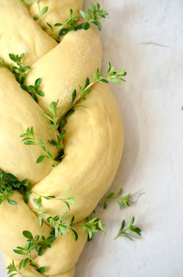 Ein Dreistrang-Zopf aus Hefeteig ist mit frischen Kräutern dekoriert und wartet auf den Backofen.